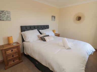 A bedroom with a double bed with white bedding two wooden bedside tables with yellow lamps and wall decor at Bothy Cottage in Embleton