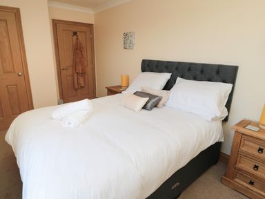A bedroom with a double bed white bedding pillows and towels wooden bedside tables with lamps and wooden doors at Bothy Cottage in Embleton