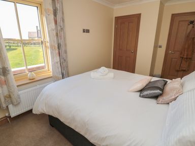 A bedroom with a bed with pillows and towels next to a window and two wooden doors at Bothy Cottage in Embleton