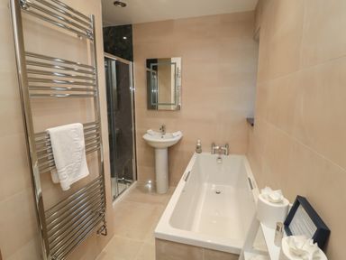 A bathroom with a bathtub pedestal sink shower and heated towel rack at Bothy Cottage in Embleton
