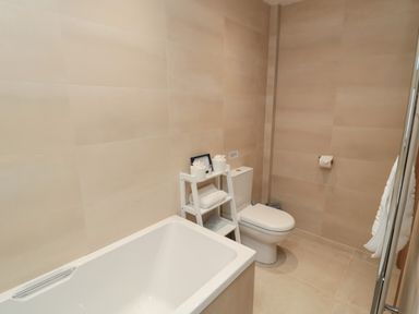 A bathroom with a bathtub toilet and a small white shelving unit holding towels and toiletries