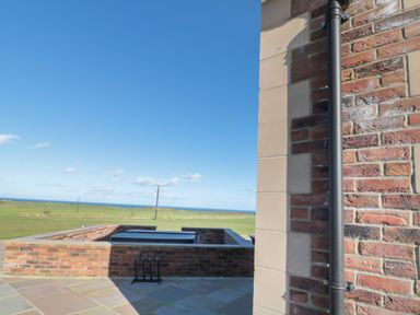 An outdoor view with brick walls a black pipe and green fields with the ocean in the distance at Bothy Cottage in Embleton