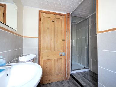 A bathroom with a wooden door a sink and a tiled shower area at The Penthouse @ No 5 in Lyme Regis