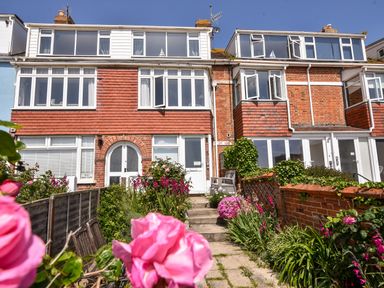 A two-story brick house with white framed windows and a garden path with flowers leading to the front door at The Penthouse @ No 5 in Lyme Regis