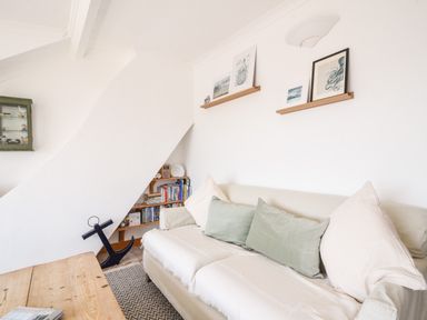 A living room with a beige sofa with cushions a wooden coffee table and wall shelves with pictures at The Penthouse @ No 5 in Lyme Regis