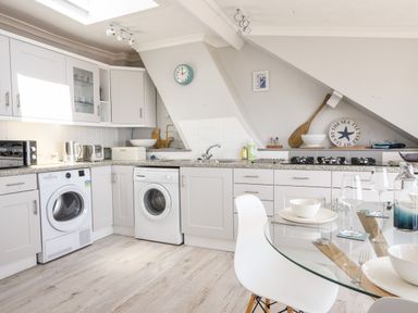 A kitchen with white cabinets two washing machines a gas stove and a glass dining table at The Penthouse @ No 5 in Lyme Regis
