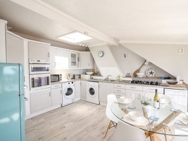 A kitchen with white cabinets a turquoise fridge washing machines a glass dining table with white chairs and kitchen appliances at The Penthouse @ No 5 in Lyme Regis