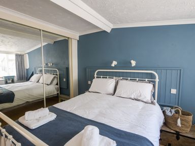 A bedroom with a double bed white linens blue blanket bedside table and mirrored wardrobe at The Penthouse @ No 5 in Lyme Regis