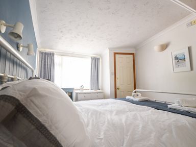 A bedroom with a bed white bedding two folded towels a white dresser blue curtains and a door at The Penthouse @ No 5 in Lyme Regis