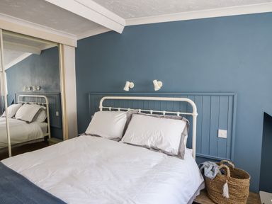 A bedroom with a double bed white bedding and pillows blue wall behind bed and a wicker basket on the floor at The Penthouse @ No 5 Lyme Regis