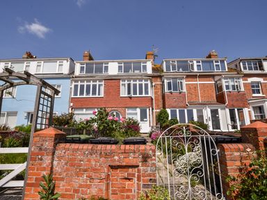 A row of brick houses with white windows and a garden with flowers behind a brick wall and white iron gate at The Penthouse @ No 5 in Lyme Regis