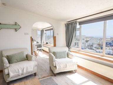A living area with two armchairs and a large window showing a street view at The Penthouse @ No 5 in Lyme Regis