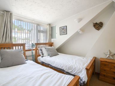 A bedroom with two single beds two wooden bedside tables and a window with vertical blinds at The Penthouse @ No 5 in Lyme Regis