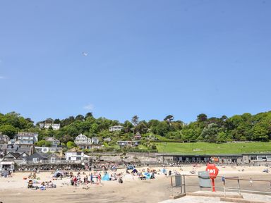A beach with people sunbathing and playing near houses and green hillside at The Penthouse @ No 5 in Lyme Regis