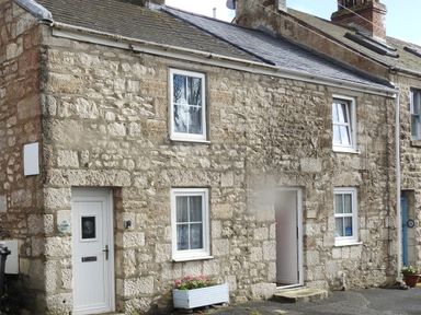 A stone cottage exterior with white framed windows and a white door with a flower box below at Pebble Reef in Easton Portland