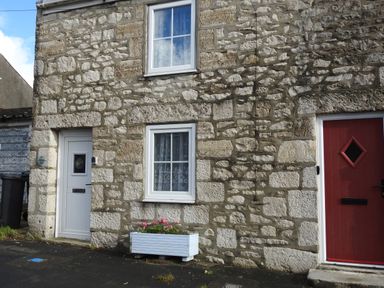 A stone exterior wall of a house with a white door a red door two windows and a white planter with flowers at Pebble Reef Easton Portland