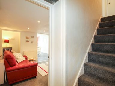A hallway with a carpeted staircase and a room with a red sofa and lamp at Pebble Reef in Easton Portland