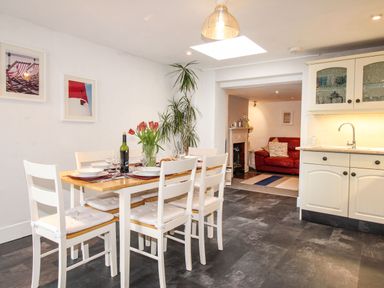A kitchen dining area with a wooden table and six white chairs near a kitchen counter and a red sofa in the adjacent room at Pebble Reef in Easton Portland