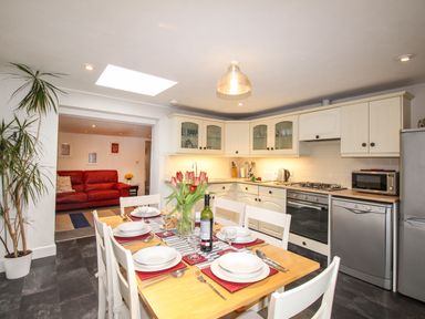 A kitchen with dining table set for six people and a living room with red sofa visible through an open doorway at Pebble Reef in Easton Portland