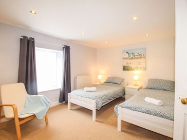 A bedroom with two single beds bedside tables with lamps a chair and a window with curtains at Pebble Reef in Easton Portland