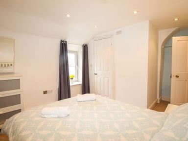 A bedroom with a bed covered in patterned bedding two rolled towels a window with dark curtains a small white dresser and two white doors at Pebble Reef in Easton Portland
