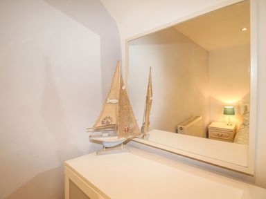 A white dresser with a decorative sailboat and a large mirror reflecting a bedside table with a lamp at Pebble Reef in Easton Portland