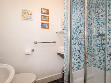 A bathroom with a shower with blue mosaic tiles a toilet a sink and framed pictures on the wall at Pebble Reef in Easton Portland