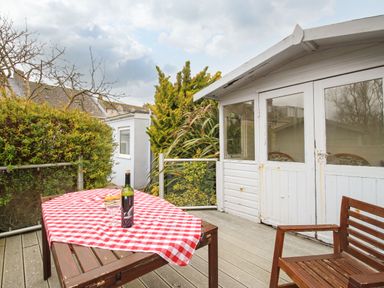 An outdoor patio with a wooden table covered with a red and white checkered cloth a wine bottle and glass with chairs and a white shed at Pebble Reef in Easton Portland