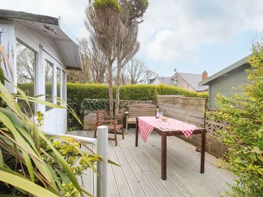 An outdoor deck with a wooden table covered with a red and white checkered cloth and wooden chairs at Pebble Reef in Easton Portland