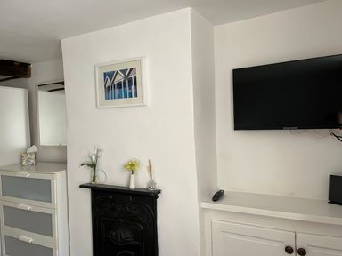 A room with a black decorative fireplace with flowers on it a white cabinet with a tissue box a wall-mounted television and a mirror on the wall at Pebble Reef in Easton Portland