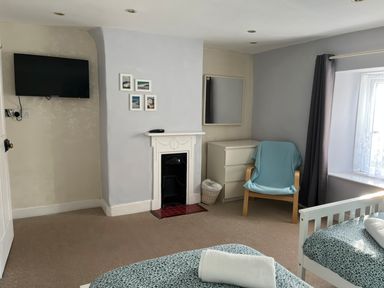 A bedroom with two single beds a fireplace a TV on the wall a wooden chair with a blue cover a white dresser and a window with curtains at Pebble Reef in Easton Portland
