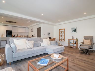 A living room with a gray sectional sofa and a wooden glass coffee table in an open plan area at 33 Cliff Edge in Newquay