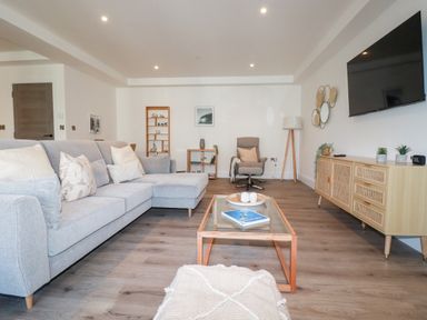 A living room with a grey sofa a glass coffee table and a TV on the wall at 33 Cliff Edge in Newquay