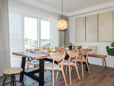 A dining room with a wooden table surrounded by chairs and a bench with a window in the background at 33 Cliff Edge in Newquay