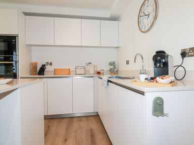 A modern kitchen with white cabinets a coffee machine a sink and wooden flooring at 33 Cliff Edge in Newquay