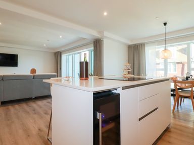 A kitchen island with a wine bottle and food trays next to a dining area and living room at 33 Cliff Edge in Newquay