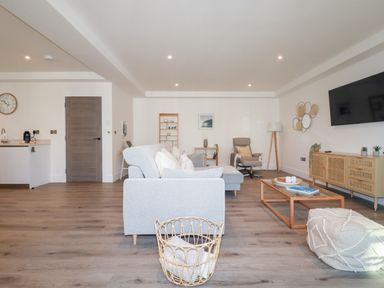 A living room with a grey sofa a wooden coffee table a wall-mounted television and a beige armchair at 33 Cliff Edge in Newquay
