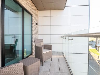 A balcony with two wicker chairs a small table and glass railing at 33 Cliff Edge in Newquay