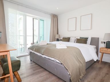 A bedroom with a bed desk stools side tables lamps and sliding glass doors at 33 Cliff Edge in Newquay