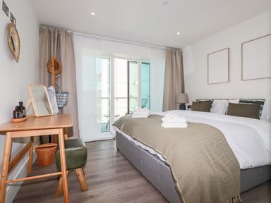 A bedroom with a large bed, desk, chair, and balcony at 33 Cliff Edge in Newquay