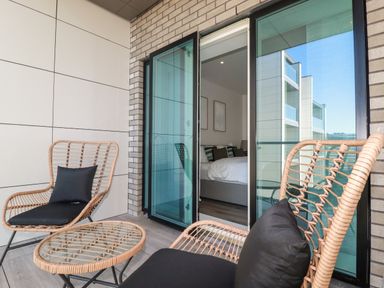 A balcony with wicker chairs and a glass table overlooking a bedroom at 33 Cliff Edge in Newquay