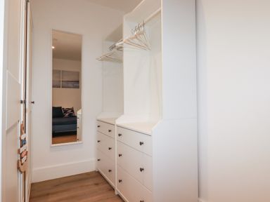 A walk-in closet with white cabinets drawers hangers and a full-length mirror at 33 Cliff Edge in Newquay