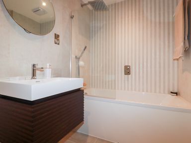 A bathroom with a sink and a bathtub with a showerhead and striped wall tiles at 33 Cliff Edge in Newquay
