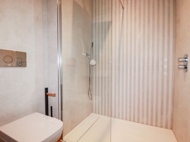 A bathroom with a white toilet and a glass-enclosed shower with striped tiles at 33 Cliff Edge in Newquay