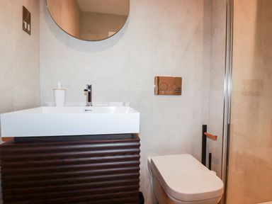 A bathroom with a sink, round mirror, toilet, and glass shower enclosure at 33 Cliff Edge in Newquay