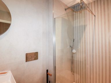A bathroom with a shower enclosure with rain shower head and handheld shower with a round mirror at 33 Cliff Edge in Newquay