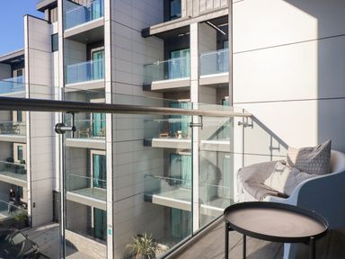 A balcony with a chair and cushions and a metal table overlooking modern apartment balconies at 33 Cliff Edge in Newquay