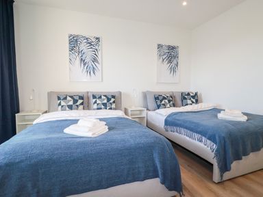 A bedroom with two beds blue blankets and pillows next to white nightstands and wall art at 33 Cliff Edge in Newquay