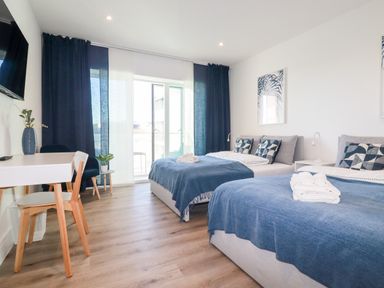 A bedroom with two beds covered with blue blankets a desk and chair and a television mounted on the wall at 33 Cliff Edge in Newquay