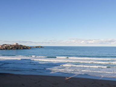 A beach with waves and people in the water with a headland and buildings in the distance at 33 Cliff Edge in Newquay